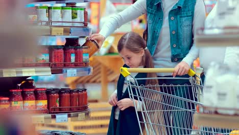 Portrait-of-a-little-girl-who-chooses-cans-in-a-supermarket-with-her-family