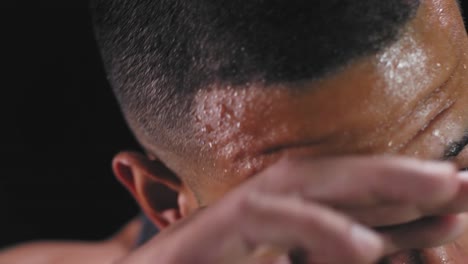 Close-up-shot-of-a-muscular-black-man-wiping-the-sweat-off-his-forehead-on-a-dark-background