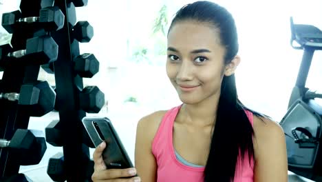 Asiatische-Frau-mit-Smartphone-im-Fitnessstudio.-Frau-Training-im-Fitness-Studio.-Sport-und-Reaktion-Konzept.-4k-Auflösung.