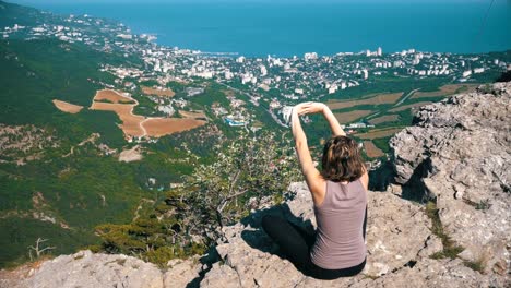 Frau-im-Lotussitz-praktizieren-Yoga-sitzen-bewegt-oder-meditiert-und-hebt-ihre-Arme-nach-oben-in-den-Bergen