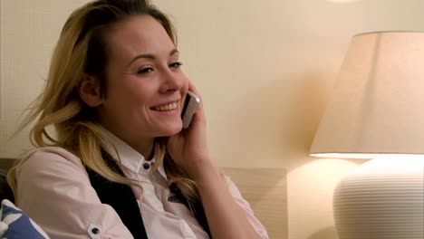 Young-woman-have-a-positive-conversation-using-mobile-phone-sitting-on-bed