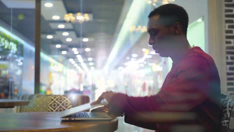 Portrait-of-happy-african-businessman-sitting-in-a-cafe-and-working-on-laptop