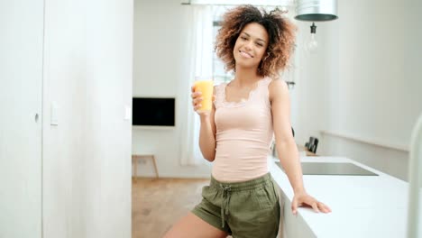 Happy-mixed-race-woman-holding-orange-juice-and-looking-to-camera.
