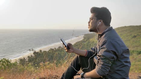 Un-joven-sentado-sobre-una-colina-viendo-y-escuchando-música-y-disfrutando-de-una-vista