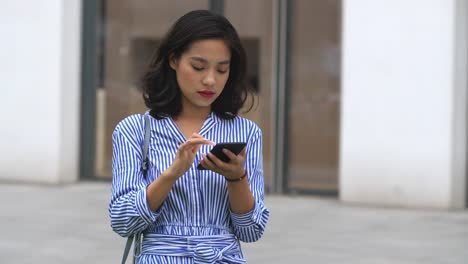 Mujer-asiática-joven-usando-el-teléfono-inteligente-en-la-calle