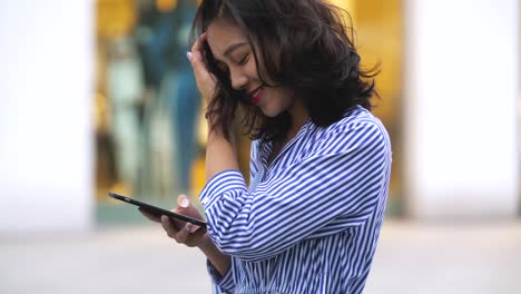 Mujer-asiática-joven-usando-el-teléfono-inteligente-en-la-calle