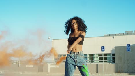 Young-woman-dancing-outside-with-smoke-grenade-at-sunset-on-rooftop-parking-garage