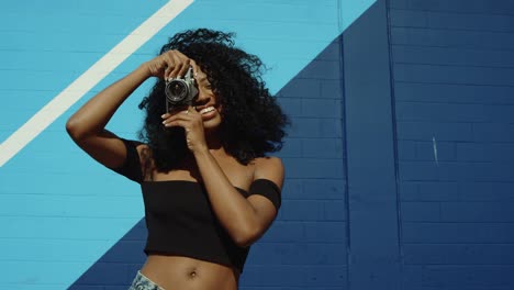 Schöne-junge-Frau-Fotografieren-mit-Film-Kamera-an-bunten-blauen-Wand