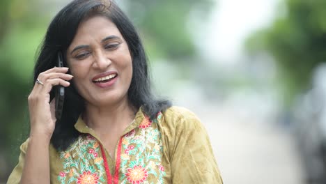 Reife-glücklich-schöne-indische-Frau-am-Telefon-beim-Denken-in-der-Straßen-Natur