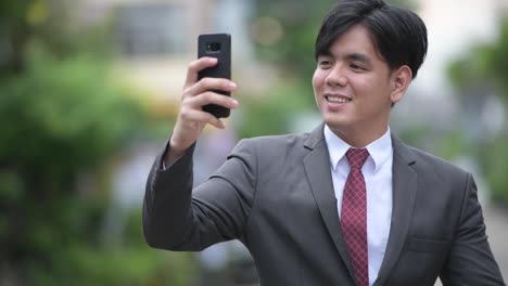 Young-handsome-Asian-businessman-using-phone-in-the-streets-outdoors