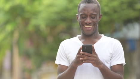 Feliz-africana-joven-sonriendo-mientras-usa-el-teléfono-en-las-calles-al-aire-libre