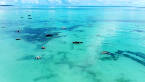 Luftaufnahme-eines-Fischers-Segel-auf-einem-Holzboot-auf-dem-klaren,-blauen-Wasser-entlang-einem-tropischen-exotischen-Strand-in-Afrika