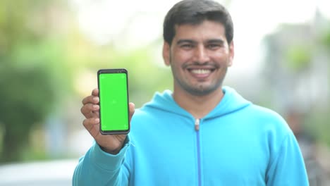 Young-happy-Persian-man-showing-phone-outdoors