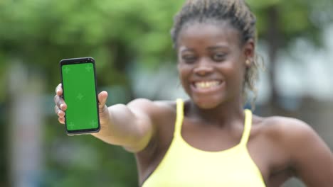 Young-happy-African-woman-showing-phone-outdoors