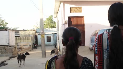 Two-women-holding-hands-and-walking-together-back-shot-handheld-mid-shot-through-streets-in-village-small-town-India-friends-bonding-together-happy-laughing-love-care-traditional-dress-streets-outdoor