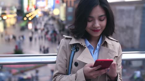 Joven-mujer-asiática-usando-teléfono-inteligente-en-la-ciudad