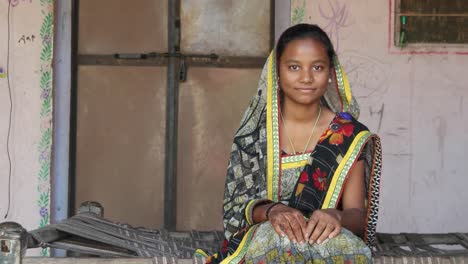 Mid-shot-of-Indian-teenager-girl-sitting-at-home-with-sari-dress-traditional-namaste-respect-covered-head-looking-at-camera-joining-henna-tattooed-hands-for-greeting-smiling-content-adjust-static