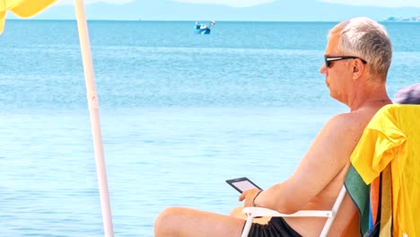 Mature-man-at-the-beach-reading-electronic-reader