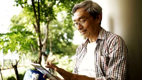 Asiatischer-senior-Mann-mit-Tablet,-allein-auf-der-Bank-im-Park-sitzen