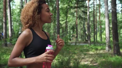 young-beautiful-African-American-woman-with-curly-hair-running-with-pink-bottle-in-a-forest