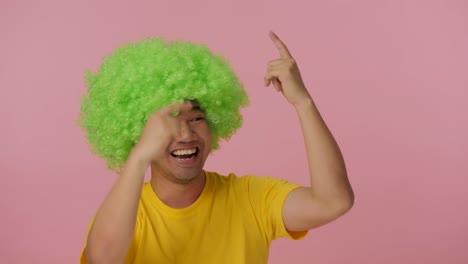 Young-crazy-man-with-colored-afro-wig-expressing-happiness-on-pink-background.