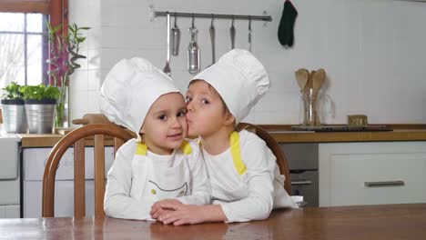 Portrait-of-two-sisters-in-the-kitchen-dressed-as-professional-chefs-who-smile-and-kisses-looking-at-the-camera-with-their-arms-folded-by-real-professional-chefs.