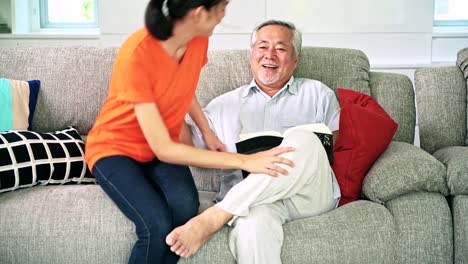 Alter-Mann-Buch-mit-seiner-schönen-Tochter-im-Wohnzimmer.-Asiatische-senior-Mann-mit-weißem-Bart-und-Asiatin.-Familie-Senior-Lifestyle-Konzept.