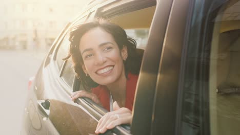 Happy-Beautiful-Woman-Riding-on-a-Back-Seat-of-a-Car,-Looks-out-of-the-Open-Window-in-Wonder-of-the-Big-City.-Traveling-Girl-Experience-Magic-of-the-World.-Camera-Shot-Made-from-Outside-the-Vehicle.