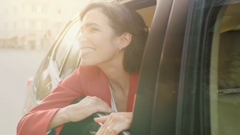 Glücklich-schöne-Frau-reitet-auf-einem-Rücksitz-eines-Autos,-Blicke-aus-dem-offenen-Fenster-in-Wunder-der-Großstadt.-Reisen-Mädchen-Erfahrung-Magie-der-Welt.-Kamera-Aufnahme-gemacht-von-außerhalb-des-Fahrzeugs.