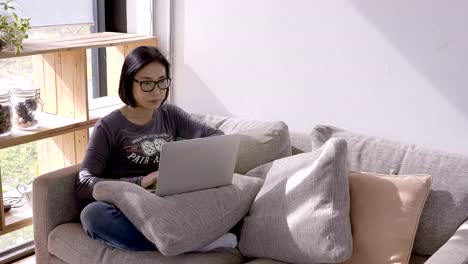 Schöne-Asiaten-junge-Frau-arbeiten-mit-Computer-Laptop-sitzend-auf-Sofa-zu-Hause.-Arbeit-zu-Hause-Konzept