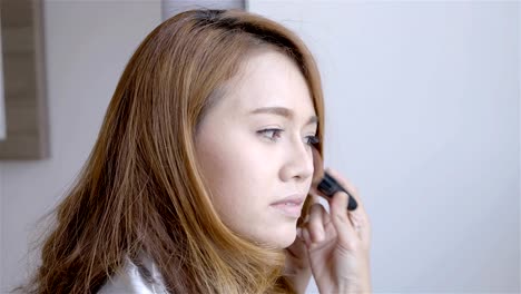 Beautiful-asian-woman-make-up-in-front-of-a-mirror-at-home-in-the-morning-bedroom.-Beauty-Concept