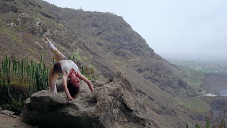 Girl-practicing-yoga-on-the-rocks-against-the-blue-sky-and-the-azure-sea.-Woman-stands-on-a-stone-in-a-bridge-posture.