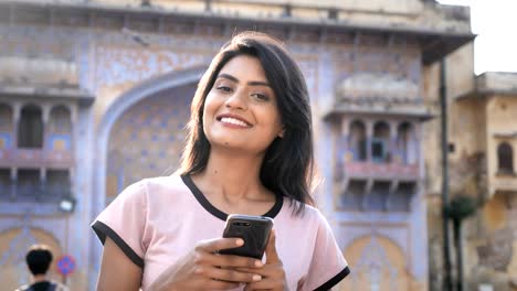 n-attractive-girl-smiling-looking-at-the-camera-on-a-city-street-holding-smartphone