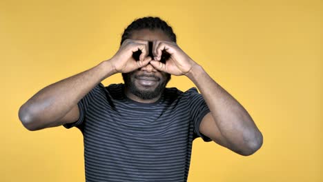 Casual-African-Man-Searching-with-Handmade-Binoculars-Isolated-on-Yellow-Background