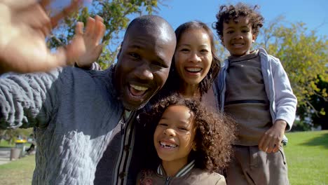 Multicultural-family-waving-and-making-video-call-together-in-park