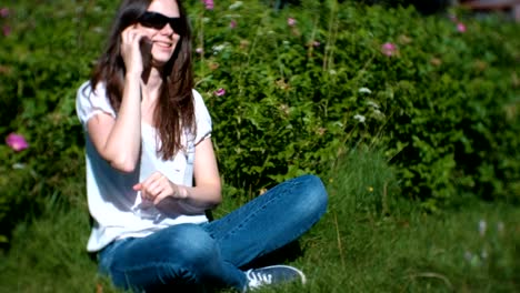 Beautiful-young-woman-is-calling-and-talking-on-mobile-phone-sitting-in-the-park.