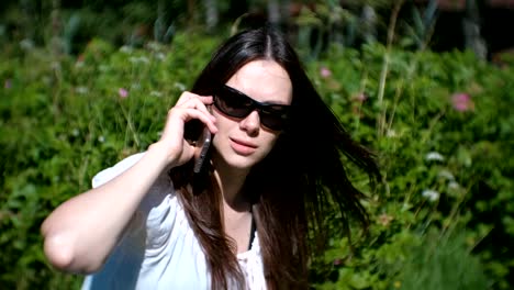 Beautiful-young-woman-is-calling-and-talking-on-mobile-phone-sitting-in-the-park.