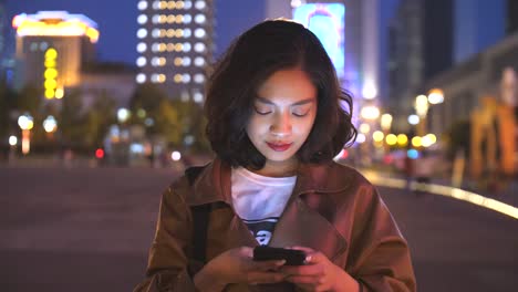 hübsche-junge-Asiatin-mit-Handy-in-der-Stadtstraße-in-der-Nacht,-4k