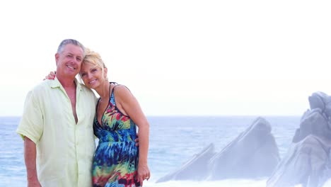 An-older-couple-kiss-each-other-on-the-beach-and-then-smile,-with-waves-crashing-on-rocks-behind-them