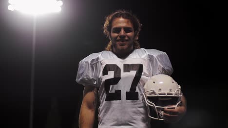 Portrait-of-a-football-player-on-a-field-holding-his-helmet