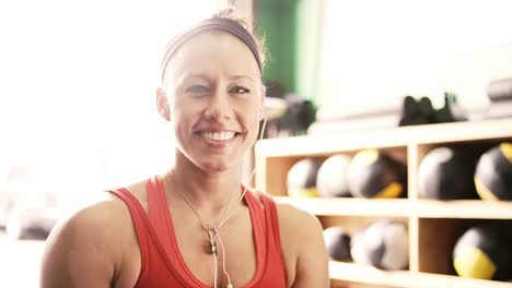 Un-ajuste-mujer-joven-en-un-pequeño-gimnasio-bebidas-de-una-botella-de-agua-y-luego-sonrisas-en-la-cámara,-acercamiento