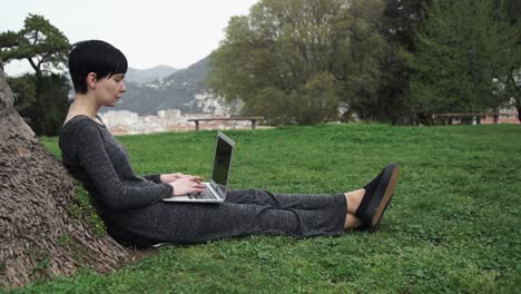 Joven-mujer-sentada-en-el-árbol-con-capacidad-para-computadora-portátil