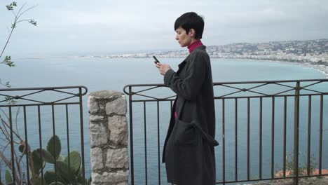 Woman-sms-texting-using-app-on-smart-phone-in-the-city-view-seashore