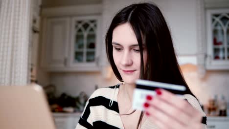 Attractive-young-smiling-woman-uses-plastic-credit-card-shopping-online-with-laptop