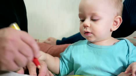 Attractive-baby-boy-draws-a-pen-with-his-grandparents-home-on-the-couch.-The-boy-stares-at-the-animals-that-drew-grandfather.-The-concept-of-different-generations