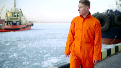 Dock-Arbeiter-in-orange-Uniform-mit-Blick-auf-das-Meer-und-Wandern-in-den-Hafen-im-Winter.-Vereisten-See