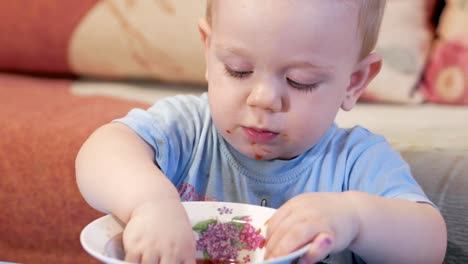 Un-atractivo-chico-de-2-años-de-edad-es-comer-sopa-roja-sí-mismo.-La-hoja-de-laurel,-atrapado-en-una-placa-y-el-niño-juega-con-él