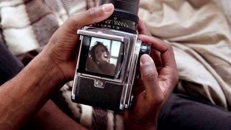 Close-up-view-of-african-man-holding-old-photocamera,-taking-photo-portrait-beautiful-woman.-Multiracial-couple-on-bed