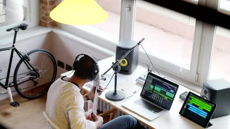 black-man-creative-musician-at-home-studio-works-by-playing,singing-and-recording-guitar-with-notebook-tablet-and-microphone-indoor-in-modern-industrial-house.-4k-handheld-top-view-overhead-video-shot