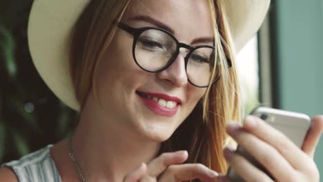 Hermosa-joven-emocional-enviar-mensajes-de-texto-en-el-teléfono-móvil.-Mujer-arruga-y-sonriendo.-Mujer-usando-Messenger-smartphone-en-café.